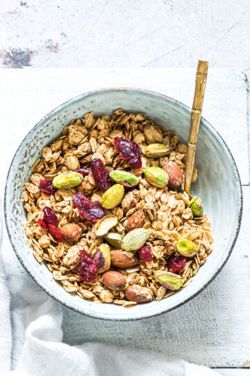 A bowl filled with granola topped with cranberries and pistachios.