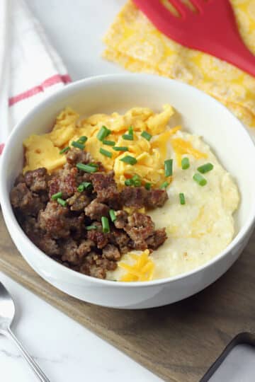 A white bowl filled with grits, sausage, and scrambled eggs.
