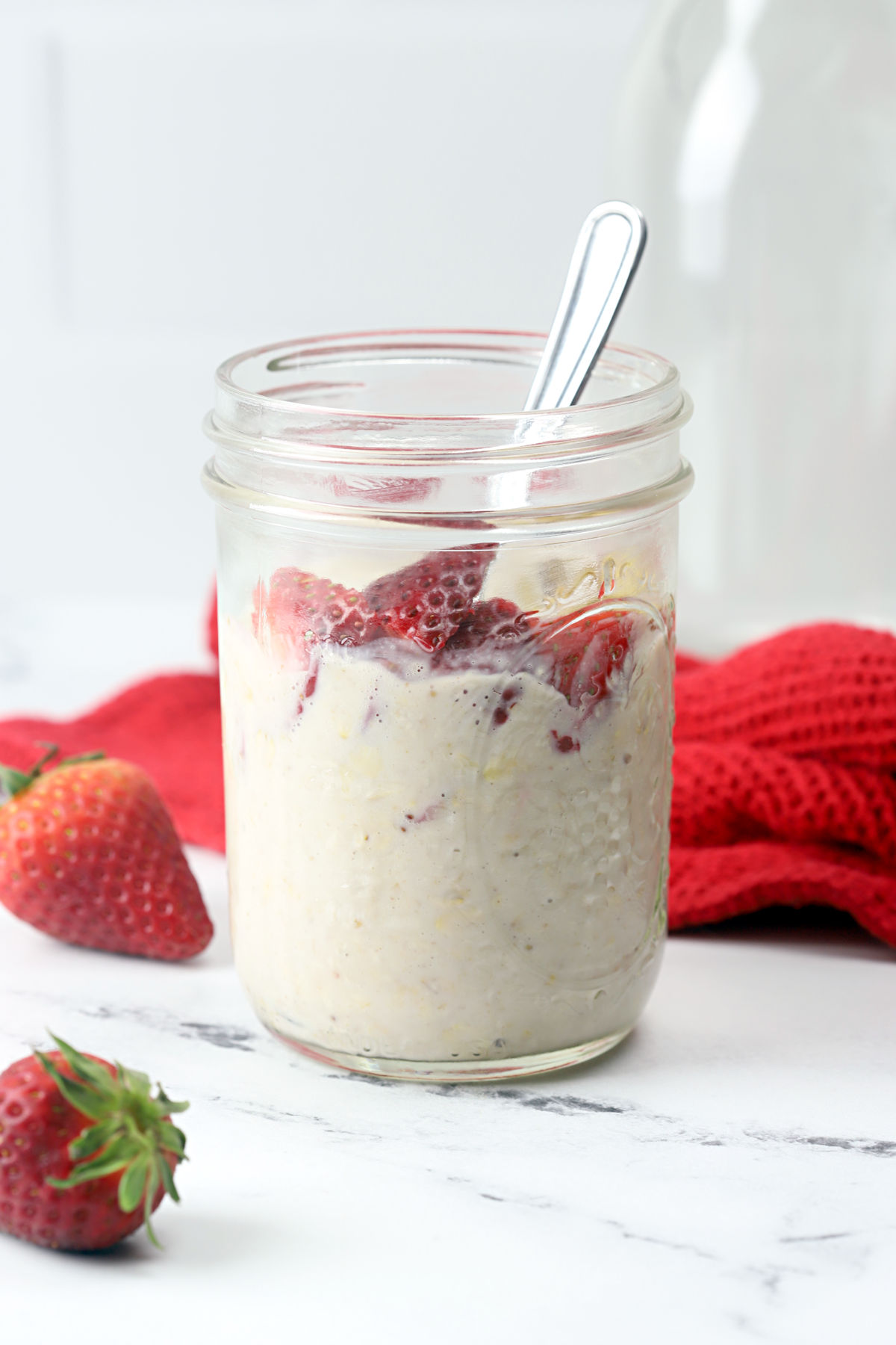 A glass jar filled with overnight oats and strawberries.