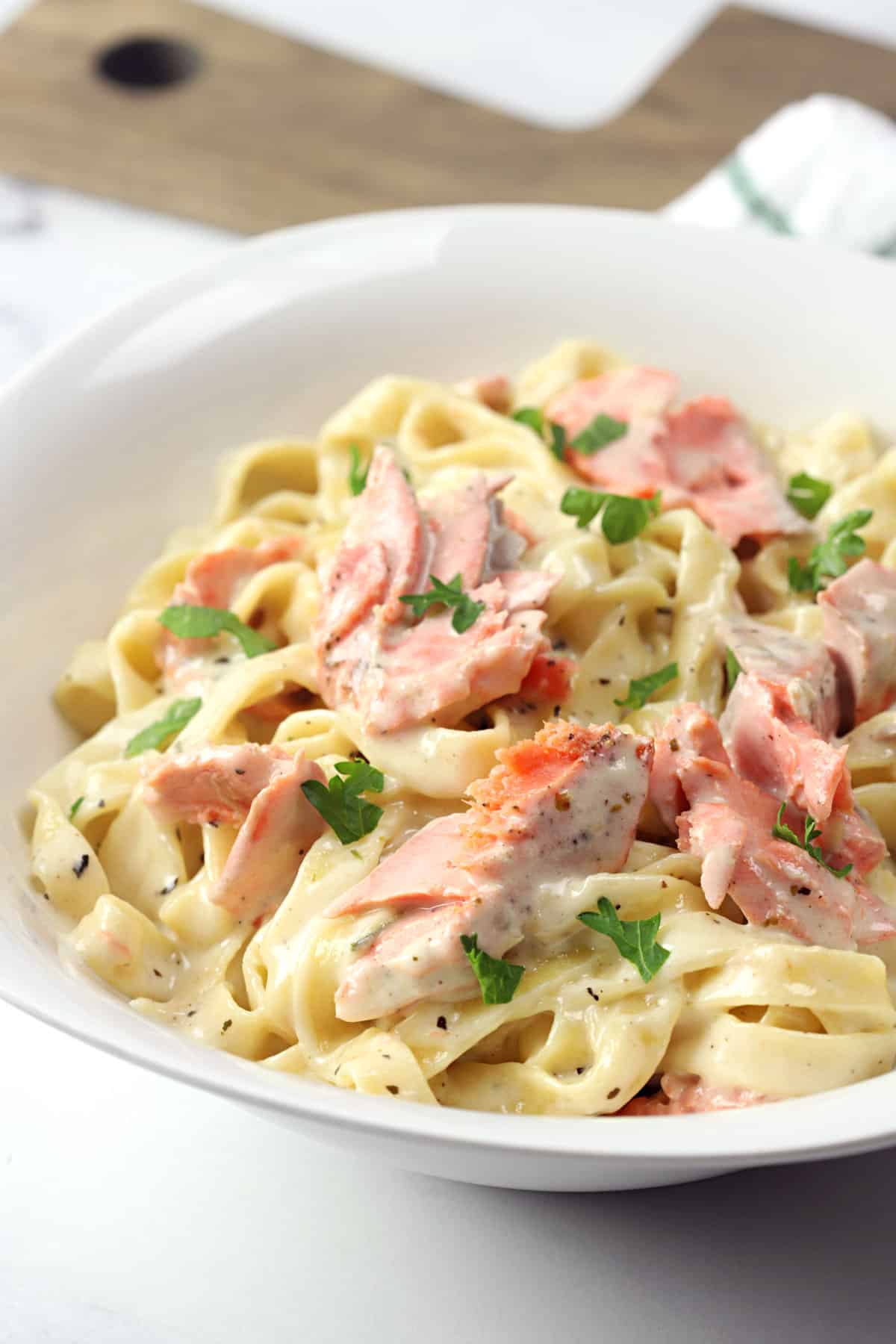A bowl of fettuccine pasta topped with flaked salmon and parsley.