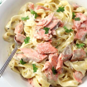 A white bowl filled with salmon alfredo and a fork.