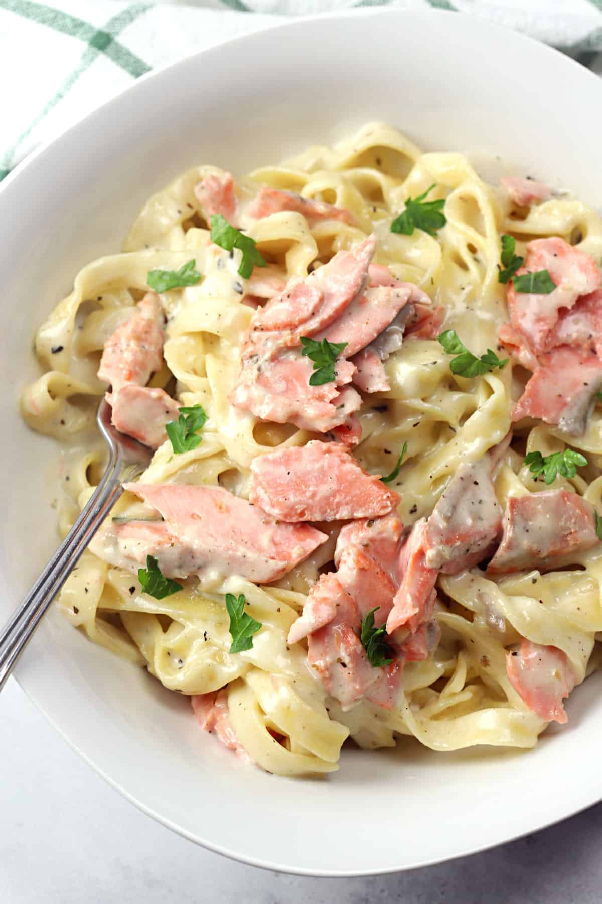 A white bowl filled with salmon alfredo and a fork.