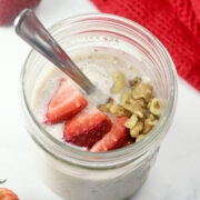 Strawberries and walnuts on top of overnight oats in a jar with a spoon.