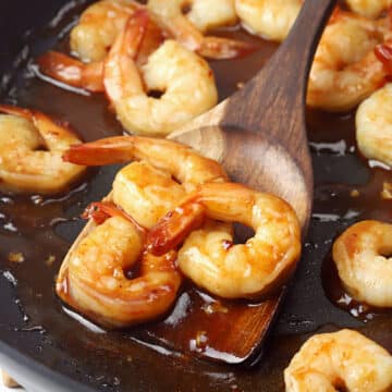 Wooden spatula scooping shrimp from a skillet.