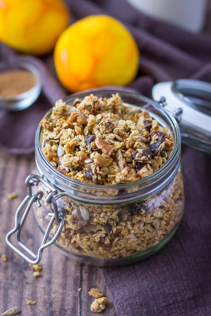A glass jar filled with granola on a wood counter top.