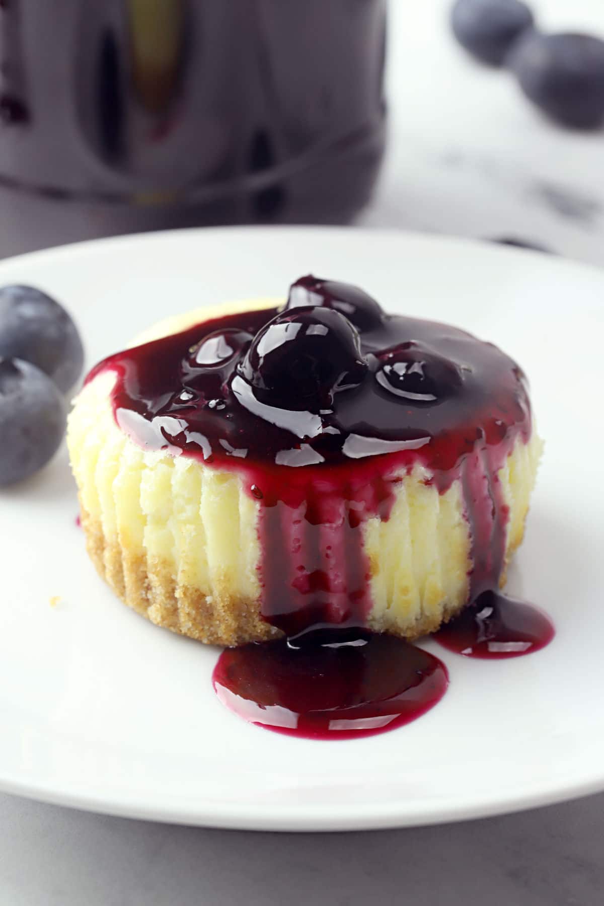 Mini cheesecake topped with blueberry sauce on a white plate.