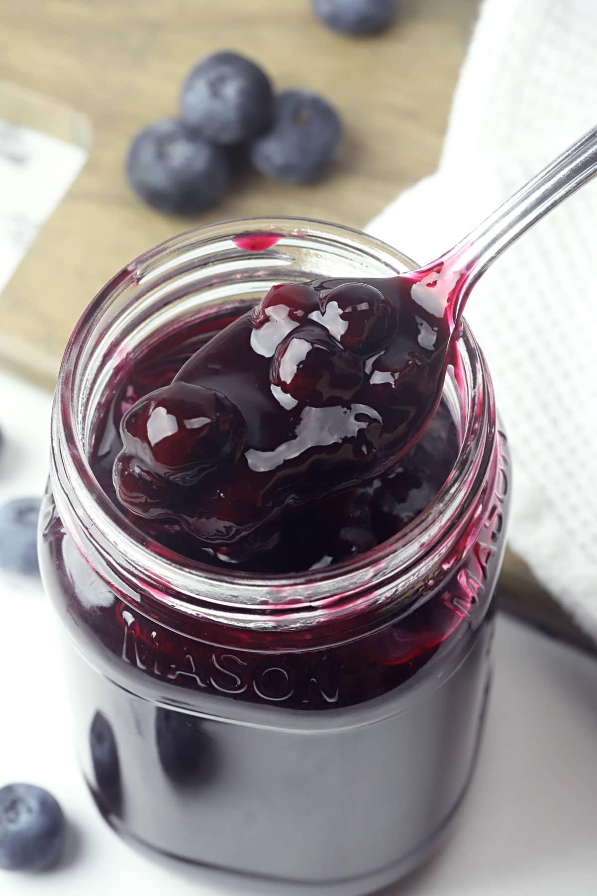 Metal spoon scooping blueberry topping from a glass jar.