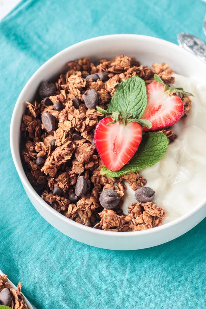 White bowl of granola topped with strawberries sitting on a blue napkin.