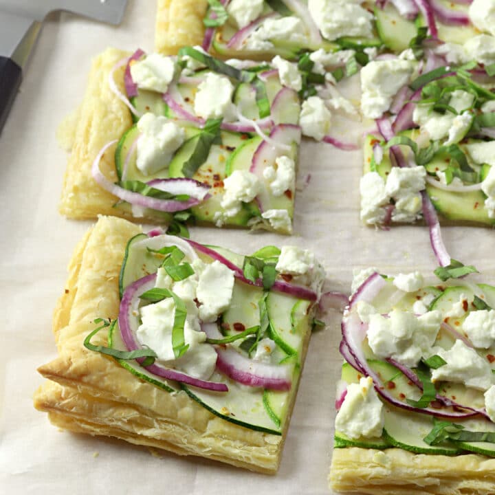 A puff pastry tart sliced into squares on a sheet of parchment paper.