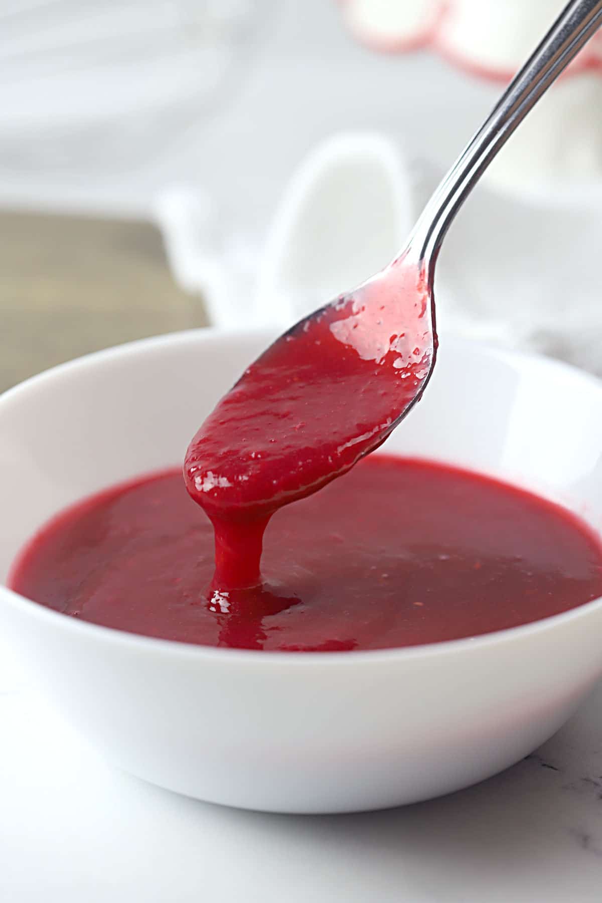 A spoon scooping raspberry sauce from a white bowl.
