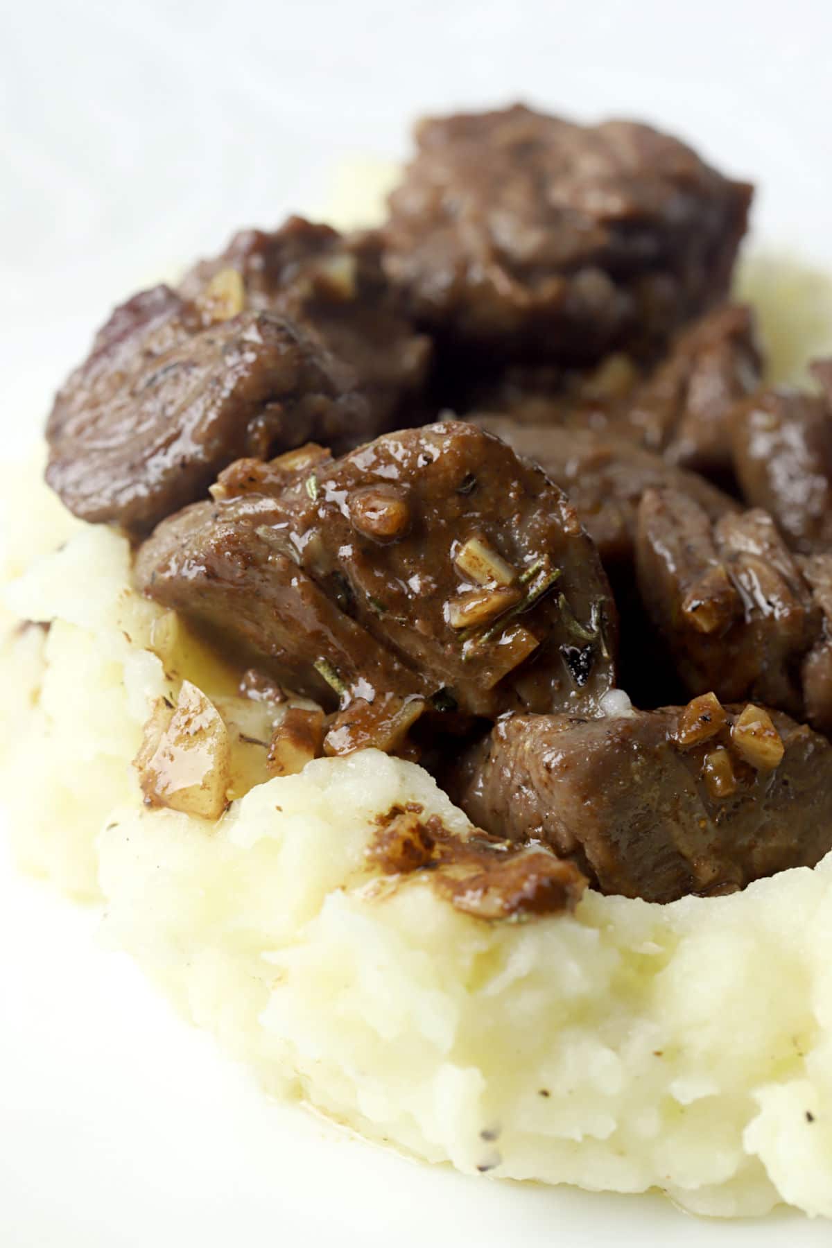 Sirloin tips sitting on a bed of mashed potatoes.