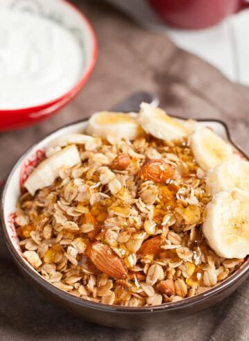 Granola in a bowl topped with sliced bananas and honey.