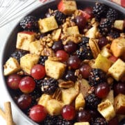 A bowl filled with fruit salad next a red and gold kitchen towel and cinnamon sticks.