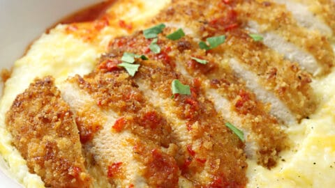 Sliced pan fried chicken on top of a bowl of cheesy grits.