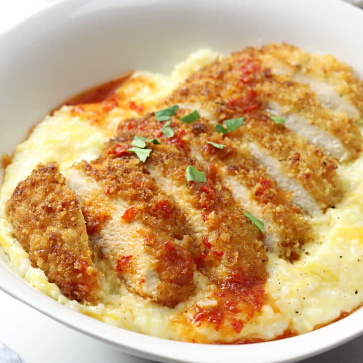 Sliced pan fried chicken on top of a bowl of cheesy grits.