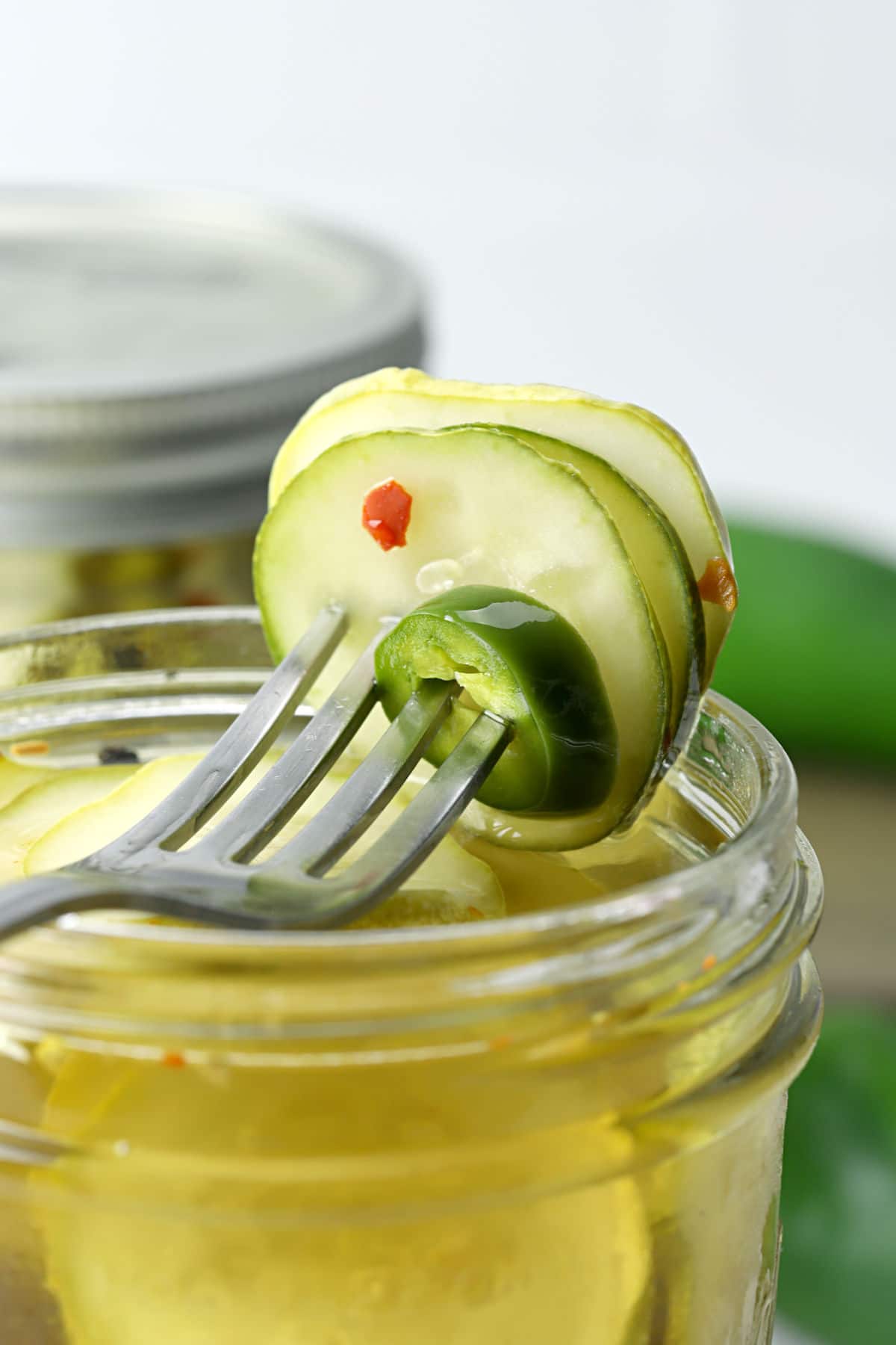 Fork piercing into sliced pickles and jalapeno on top of a jar.