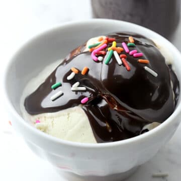 Hot fudge and rainbow sprinkles poured over a bowl of vanilla ice cream.