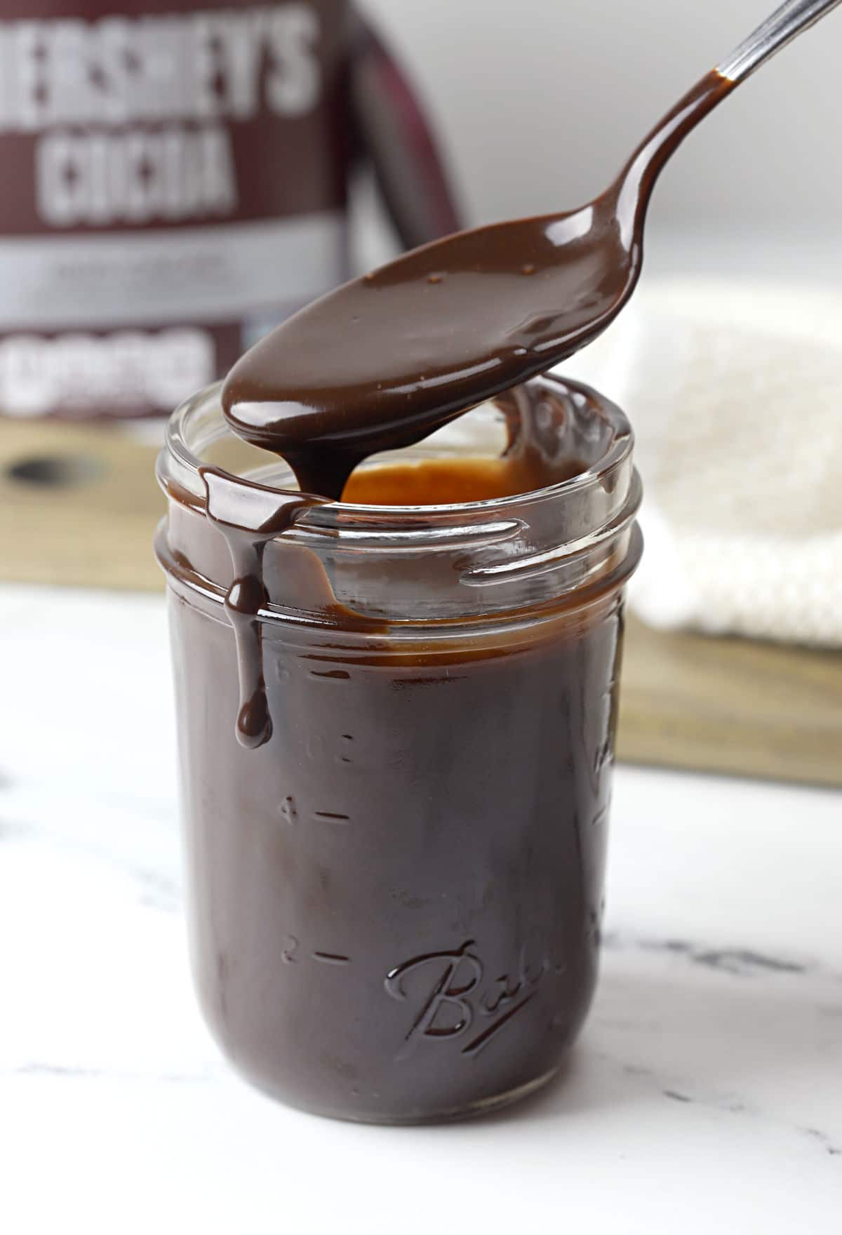 A metal spoon scooping hot fudge out of a glass jar.