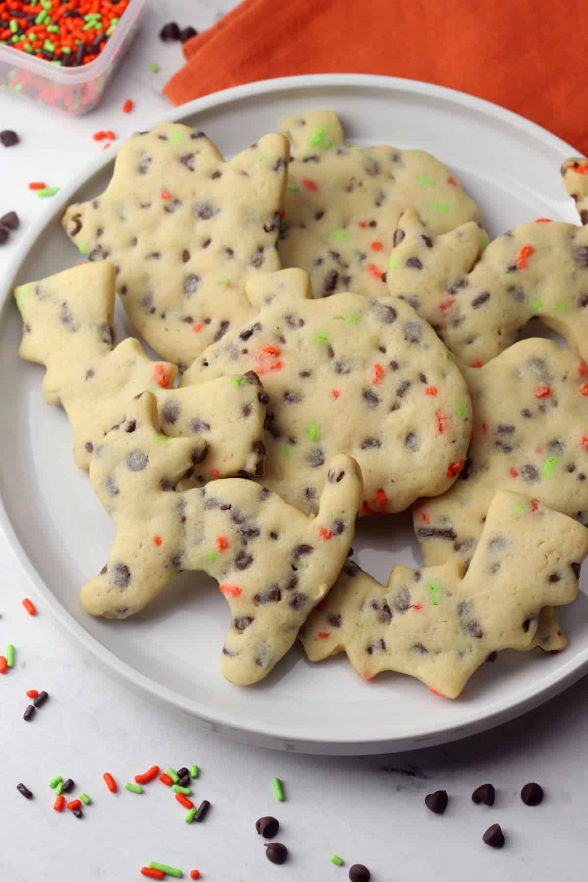 A white plate filled with chocolate chip cut out cookies shaped like cats, pumpkins, and bats.