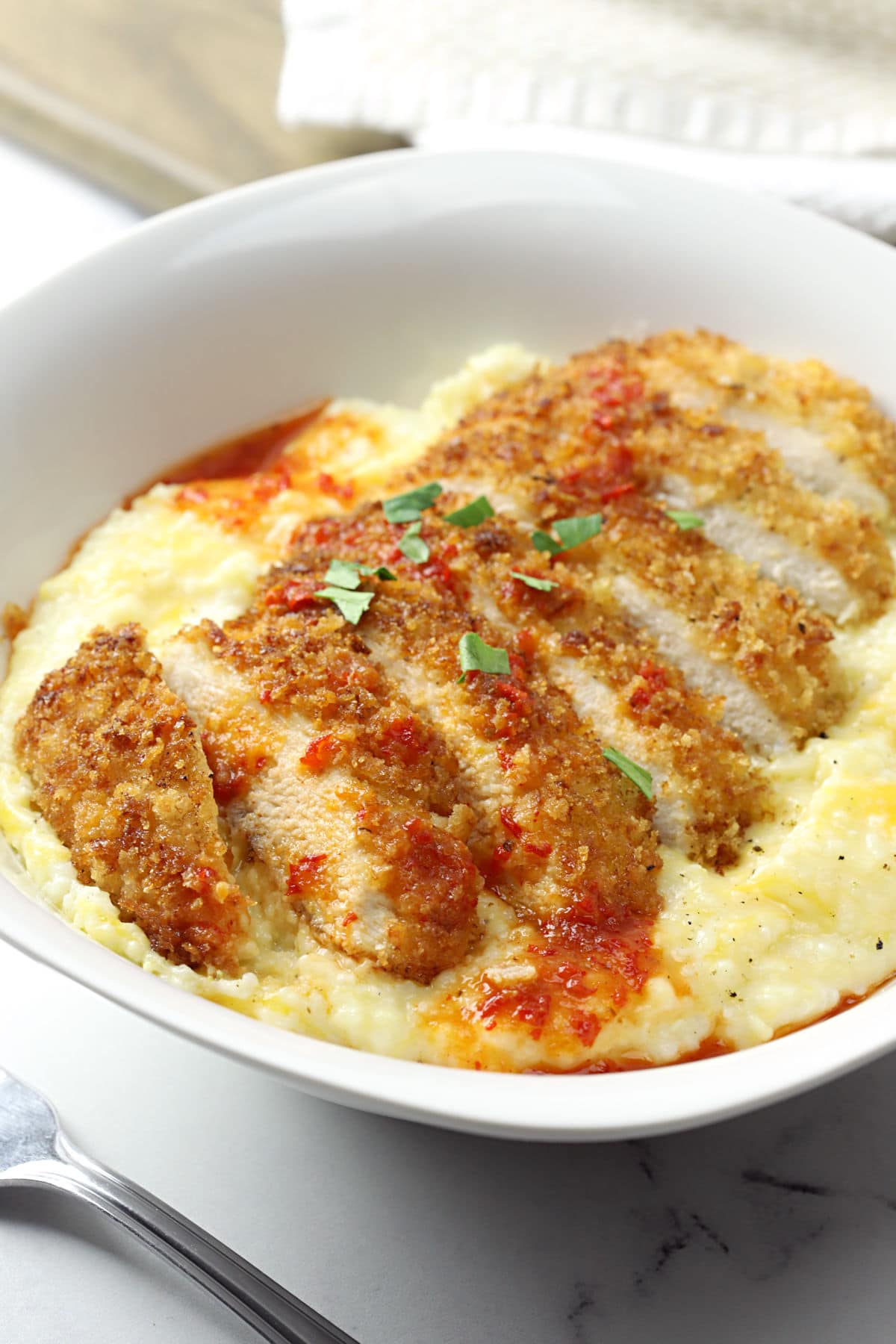 Sliced pan fried chicken on top of a bowl of cheesy grits.