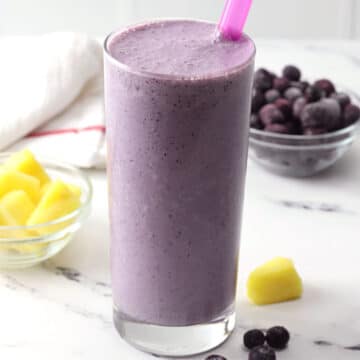 A glass filled with blueberry pineapple smoothie on a marble counter top.