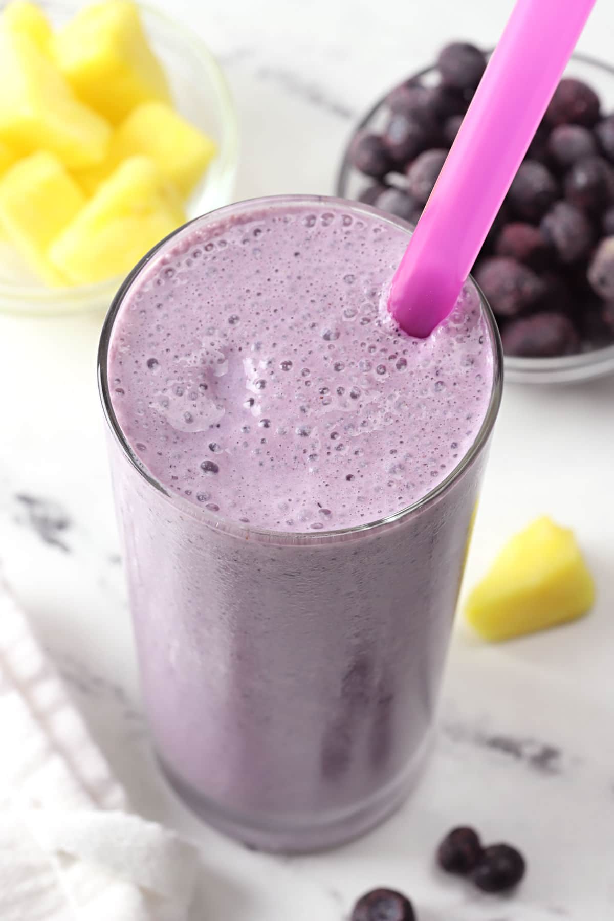 A purple smoothie in a glass with a purple straw.
