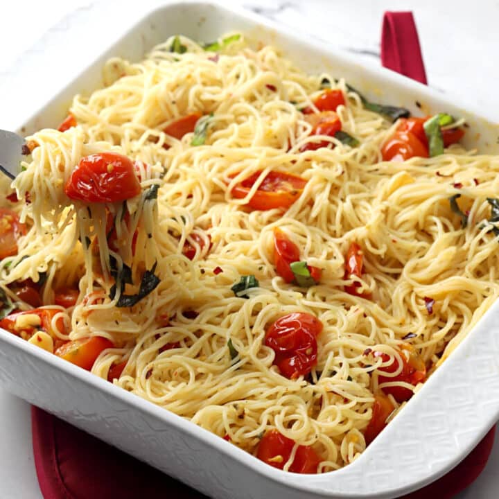 A white casserole dish filled with roasted cherry tomato pasta.