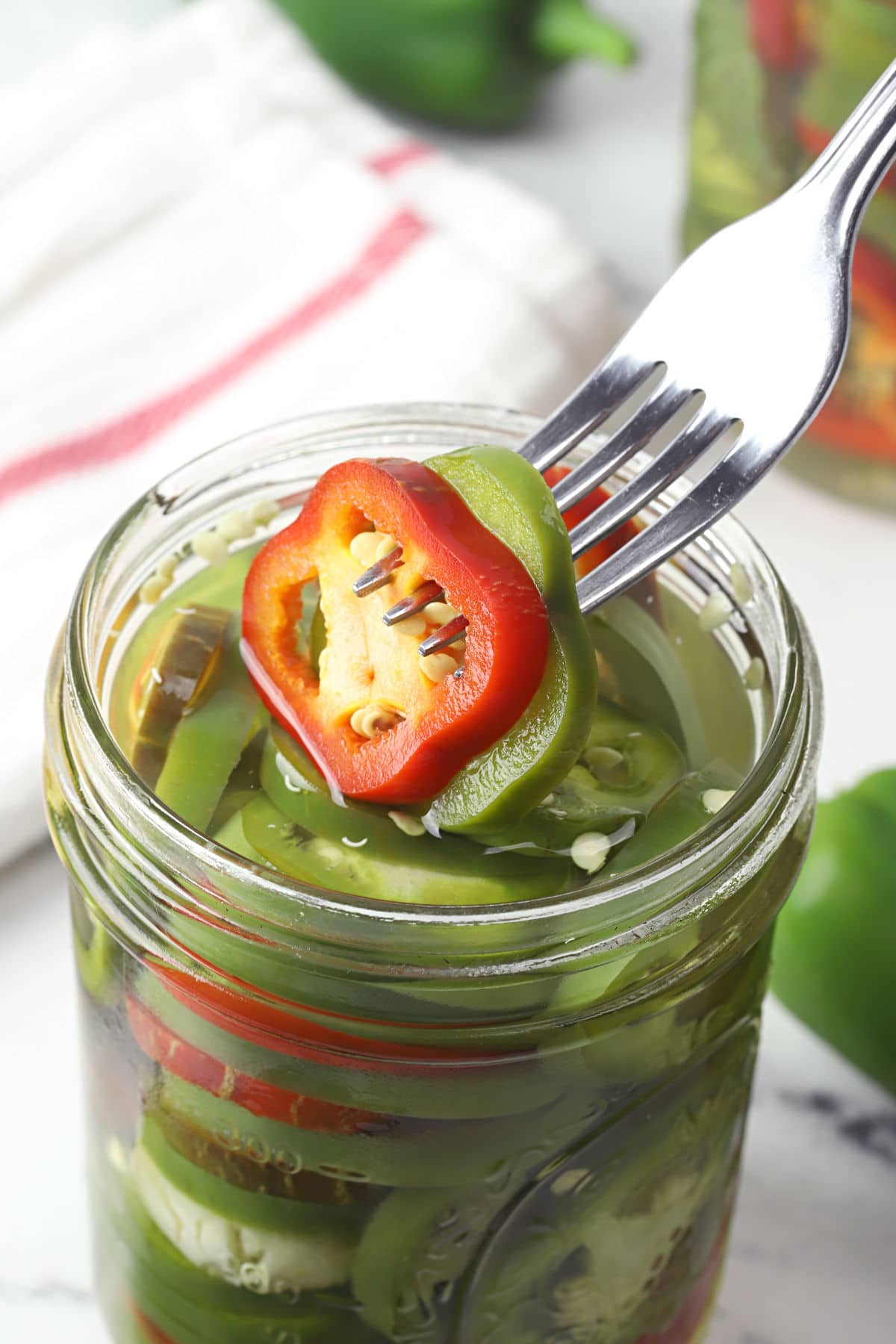 Fork lifting jalapeno slices from a jar.