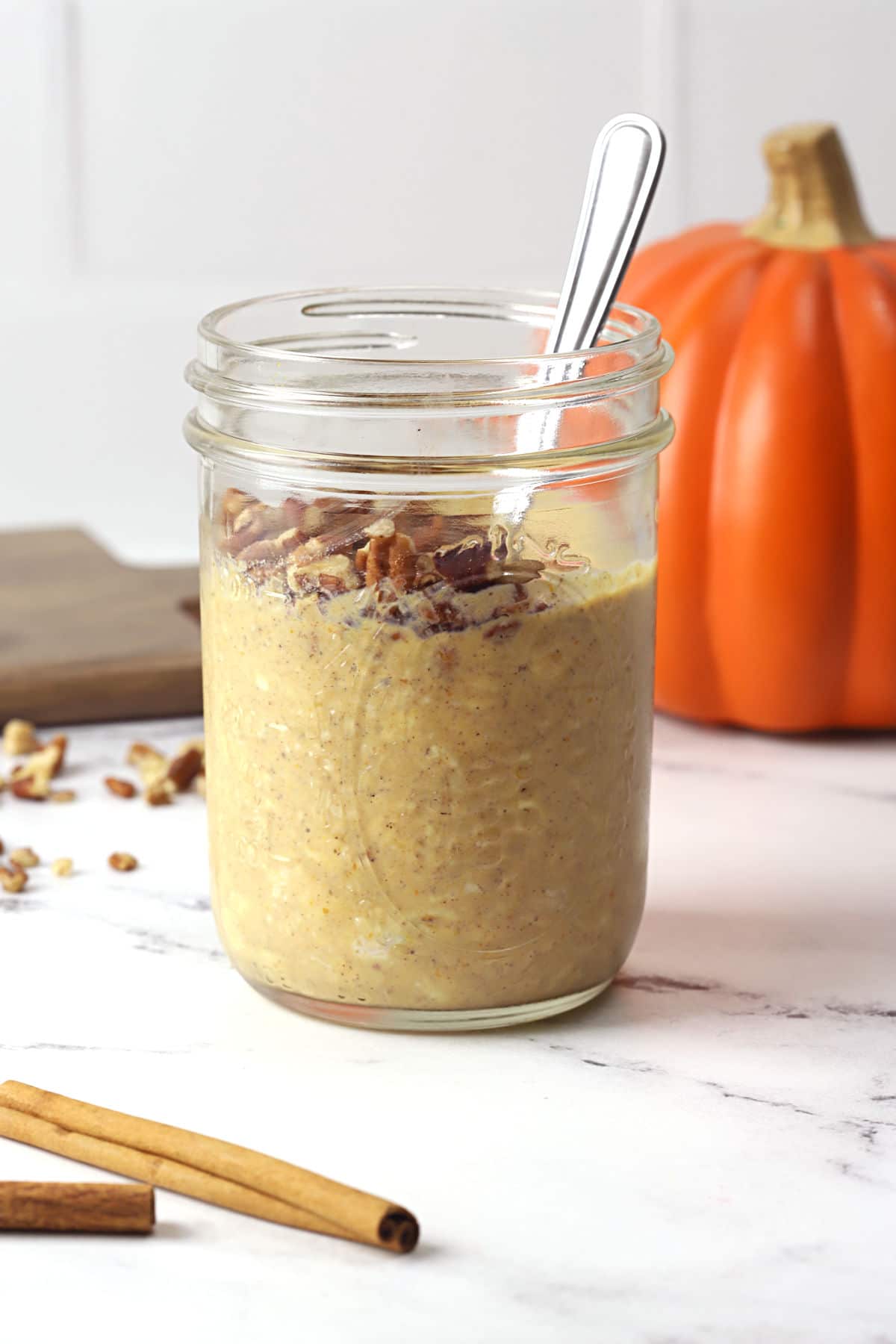 A glass jar filled with pumpkin overnight oats and a metal spoon.