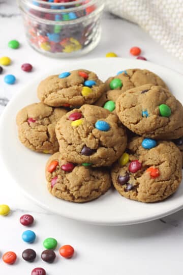 A white plate filled with small peanut butter cookies filled with colorful candies.