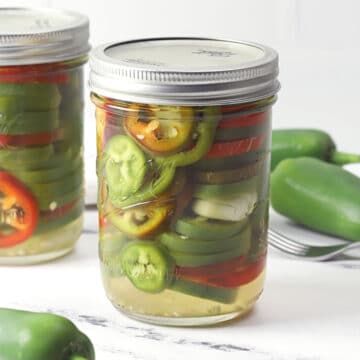 A jar of pickled jalapenos on a marble counter top.