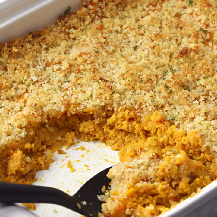 A black serving spoon scooping sweet potato casserole from a white dish.