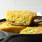 A wedge of jalapeno cornbread sitting on top of a cast iron pan.
