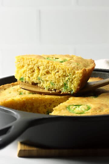 A wedge of jalapeno cornbread sitting on top of a cast iron pan.