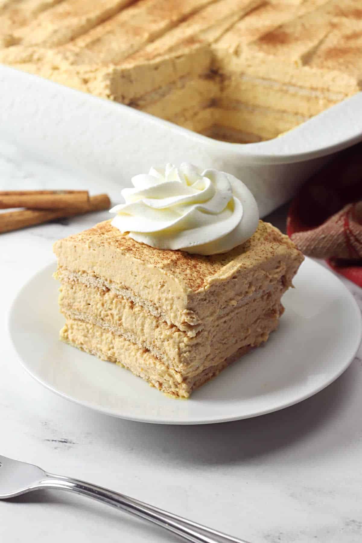 A slice of pumpkin icebox cake topped with whipped cream on a white plate.