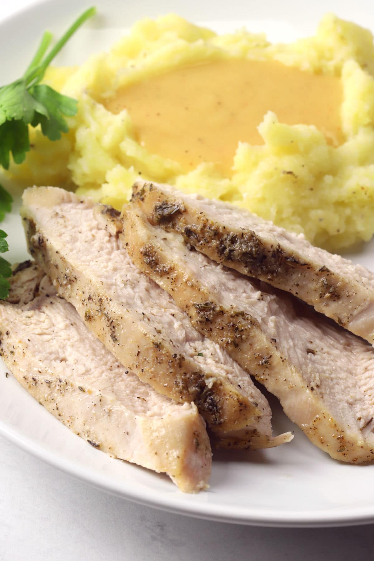 Slices of roasted turkey on a plate next to mashed potatoes.