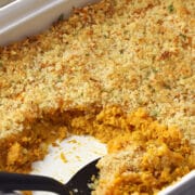 A black serving spoon scooping sweet potato casserole from a white dish.
