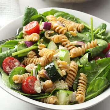 White bowl filled with spinach, pasta, and veggies.