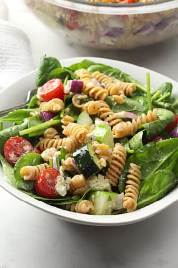 White bowl filled with spinach, pasta, and veggies.