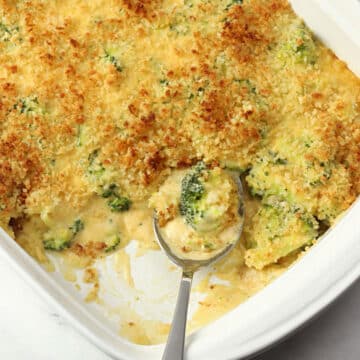 Metal spoon scooping broccoli casserole from a white casserole dish.