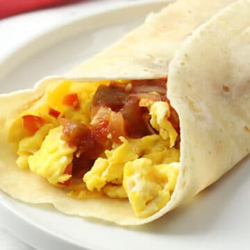 A tortilla rolled up with scrambled eggs and salsa inside.