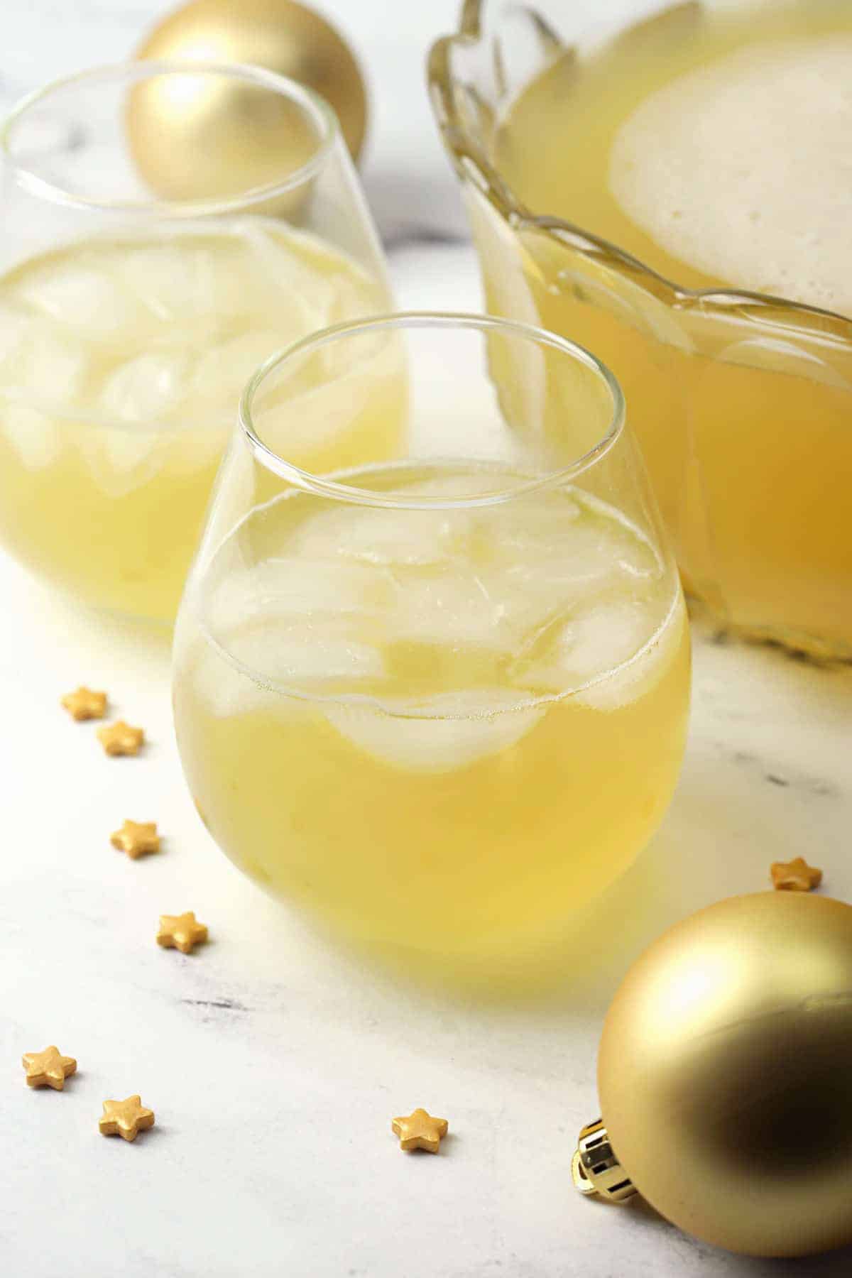 A glass of gold punch surrounded by gold star confetti and a punch bowl.