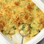 Metal spoon scooping broccoli casserole from a white casserole dish.