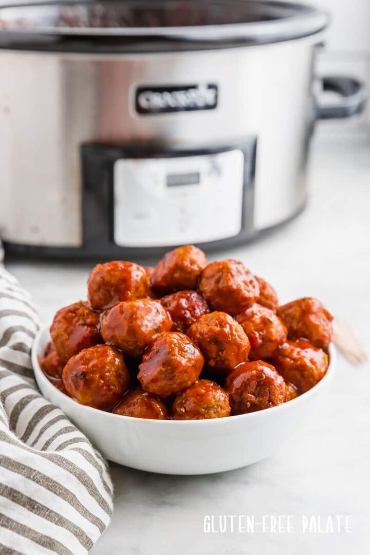 Crockpot meatballs in a white bowl with a slow cooker in the background.