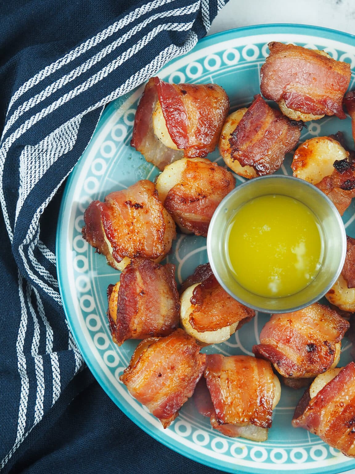 Bacon wrapped scallops on a blue plate.