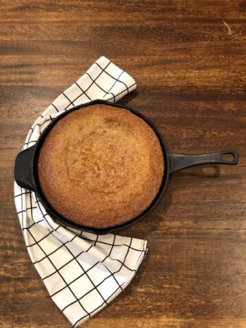 Cast iron skillet filled with banana bread with a towel on a counter top.