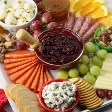 Meats, cheeses, and a bowl of cranberry sauce arranged on a sheet pan.
