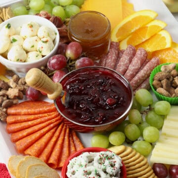Meats, cheeses, and a bowl of cranberry sauce arranged on a sheet pan.