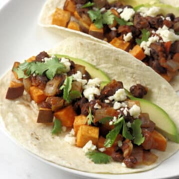 Roasted sweet potatoes and black beans served on two flour tortillas on a white plate.