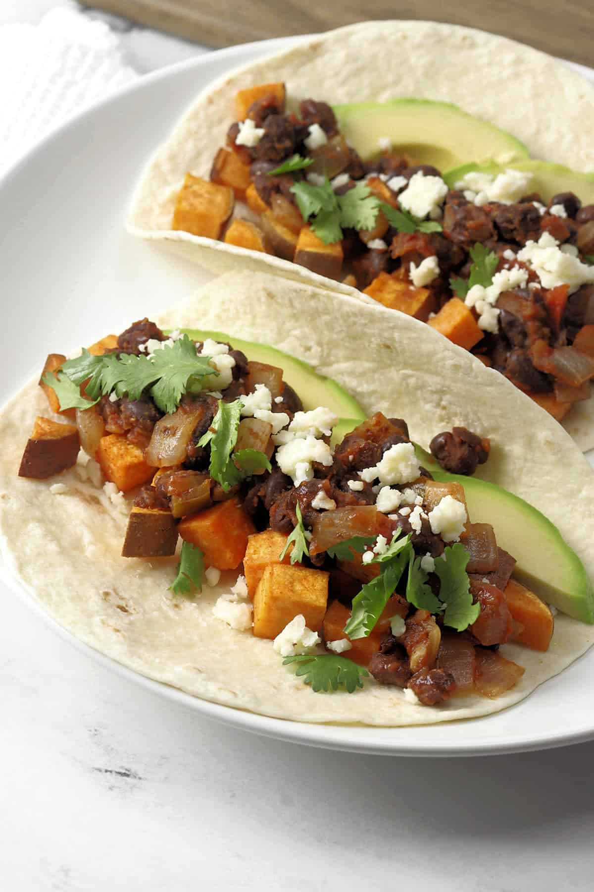 Roasted sweet potatoes and black beans served on two flour tortillas on a white plate. 